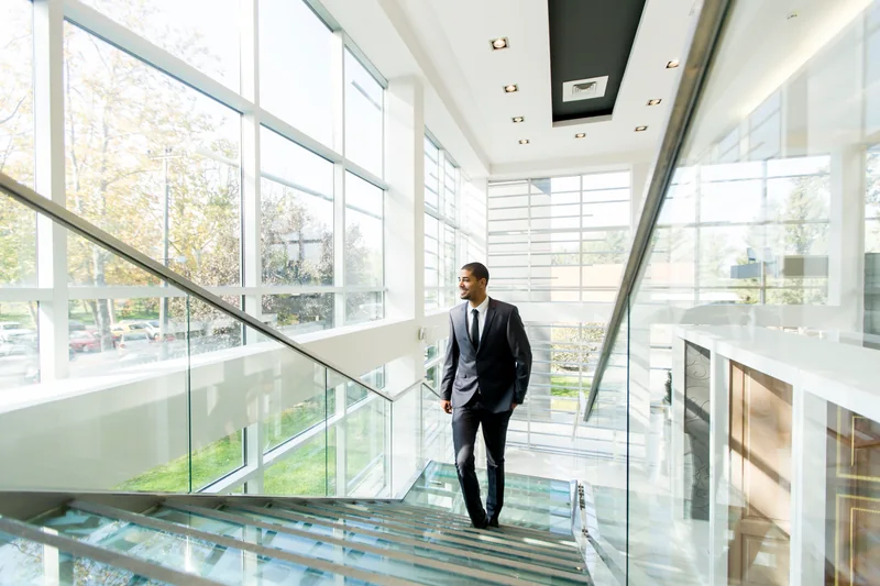 Un professionnel descend un escalier dans un immeuble de bureaux lumineux.