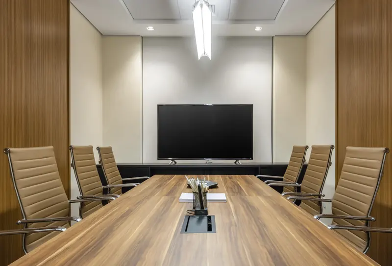 Salle de conseil avec une longue table en bois et un écran de présentation.